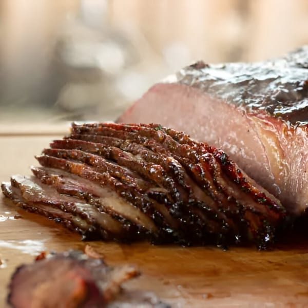 Close-up of sliced, smoked brisket with a dark, glistening crust and pink interior on a wooden board.