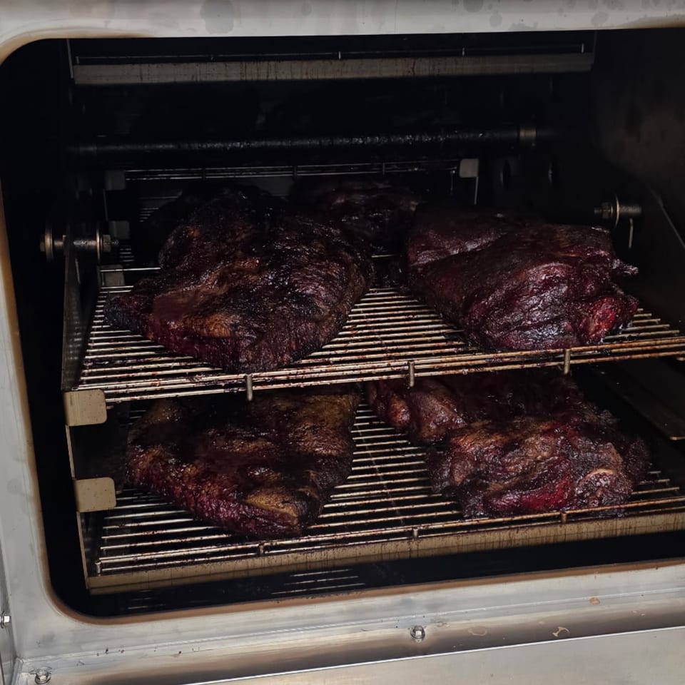 Dark, smoked brisket and other meats cooking on racks inside a large BBQ smoker.