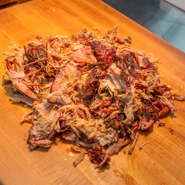Close-up of a pile of freshly pulled, juicy Arctic Smokehouse BBQ pork on a wooden cutting board.