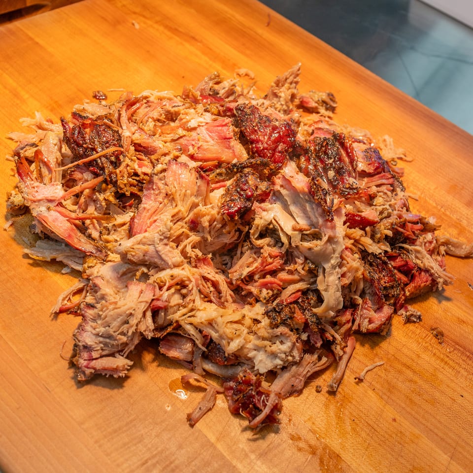 Close-up of a pile of freshly pulled, juicy Arctic Smokehouse BBQ pork on a wooden cutting board.
