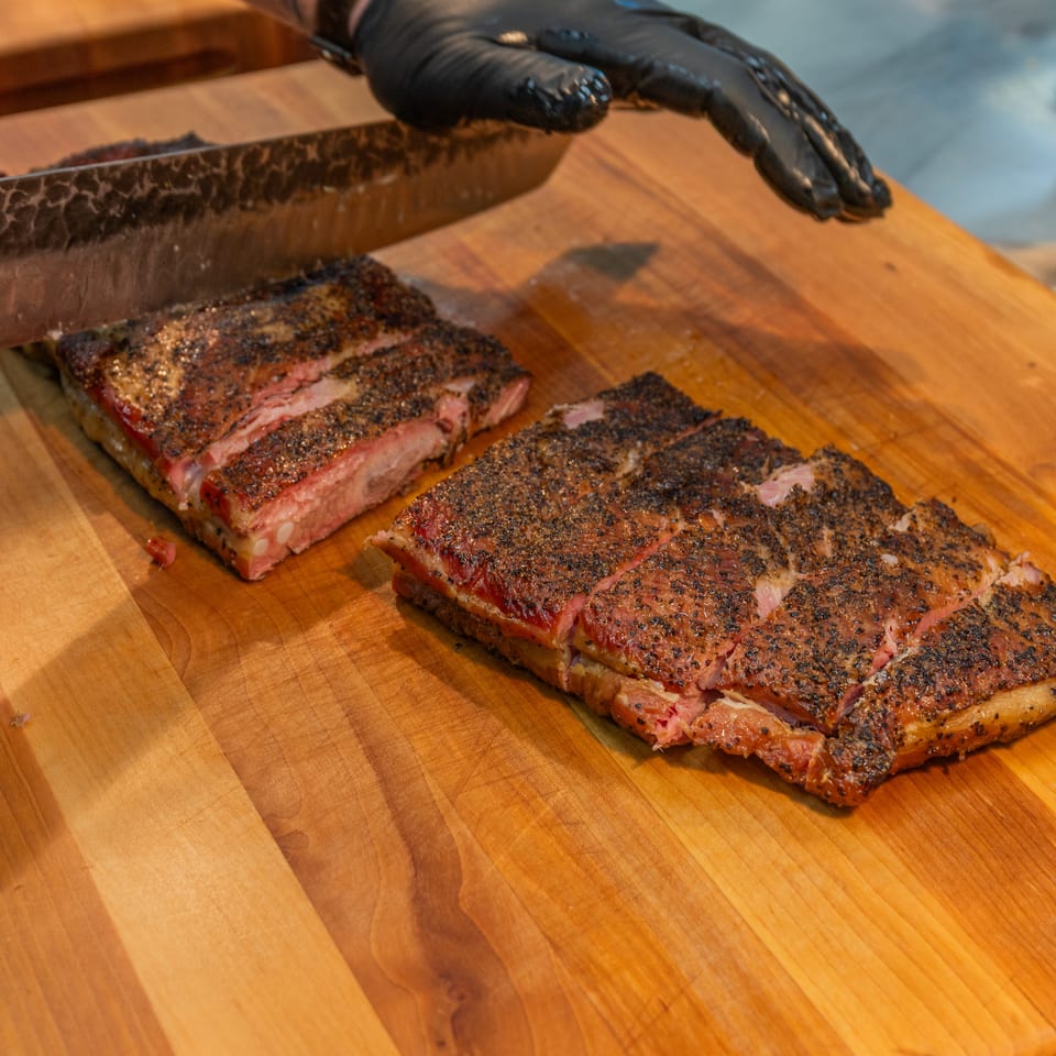 Gloved hands slicing Arctic Smokehouse BBQ brisket on a wooden cutting board.