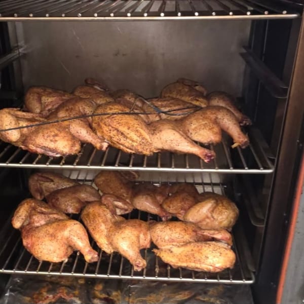 Whole chickens, seasoned and cooking on two racks inside a smoker at Arctic Smokehouse BBQ.