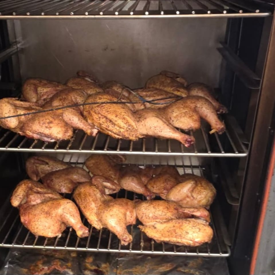 Whole chickens, seasoned and cooking on two racks inside a smoker at Arctic Smokehouse BBQ.