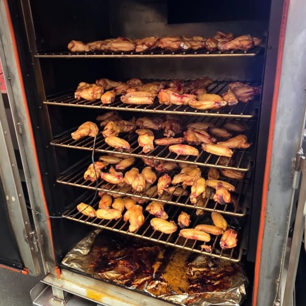 Chicken wings cooking on multiple racks inside a large, dark smoker at Arctic Smokehouse BBQ.